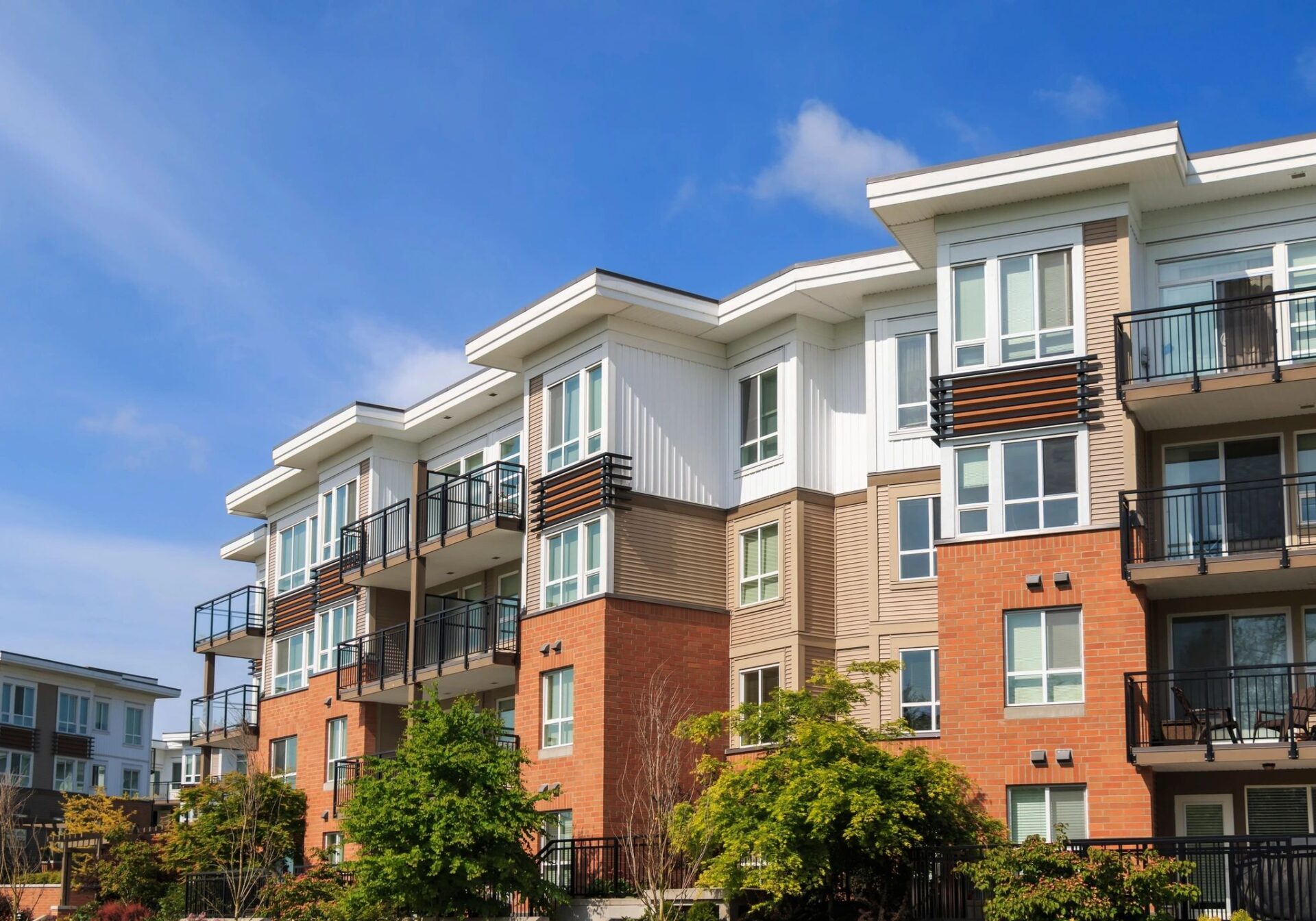 A row of apartment buildings with trees in front.